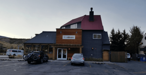 A two-story building with a red roof and wooden accents, featuring a parking lot and surrounding trees.