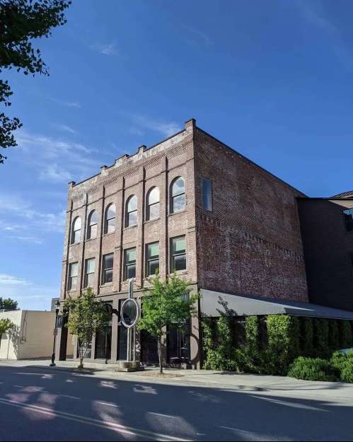 Historic brick building with arched windows, greenery in front, under a clear blue sky.