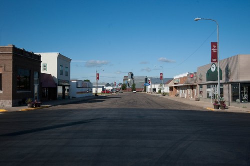A quiet street in a small town, lined with shops and buildings under a clear blue sky.