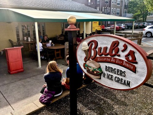 A sign for Bub's Burgers & Ice Cream outside a restaurant with outdoor seating and customers enjoying their meals.