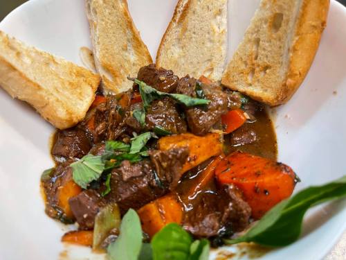 A bowl of hearty beef stew with carrots and herbs, accompanied by toasted bread slices.