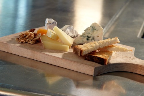 A wooden board with various cheeses, nuts, dried fruit, and slices of bread arranged on a metallic surface.