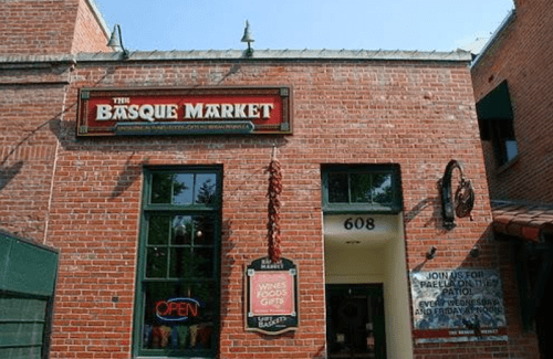 Exterior of The Basque Market, featuring a brick facade, open sign, and a welcoming entrance.