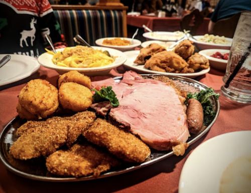 A festive table spread featuring a platter of ham, fried chicken, pasta, and various side dishes.