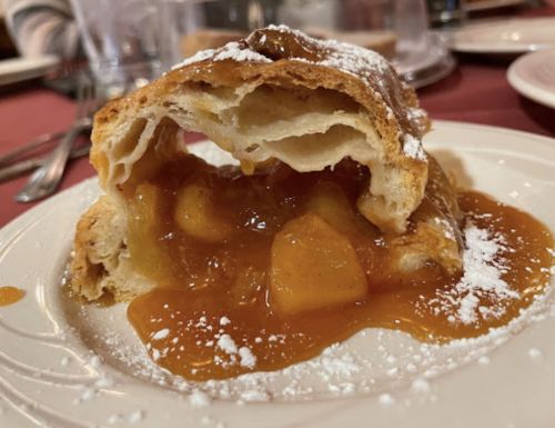 A flaky pastry filled with warm apple filling, dusted with powdered sugar, served on a plate.