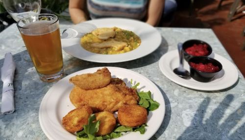 A plate of fried fish and hushpuppies on a table with a beer and a bowl of soup in the background.