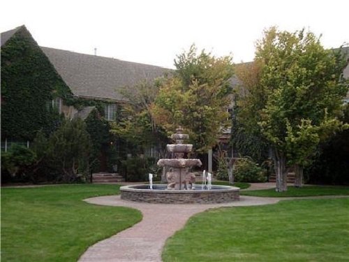A landscaped courtyard featuring a stone fountain surrounded by trees and a grassy area.