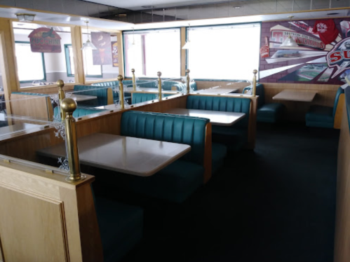 Interior of a diner featuring teal booths, wooden tables, and large windows, creating a cozy atmosphere.