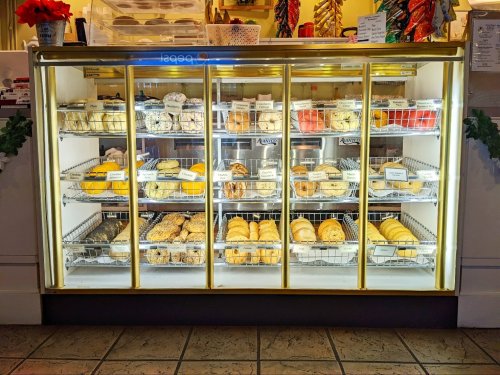 A display case filled with various baked goods, including cookies, pastries, and bread, in a cozy bakery setting.