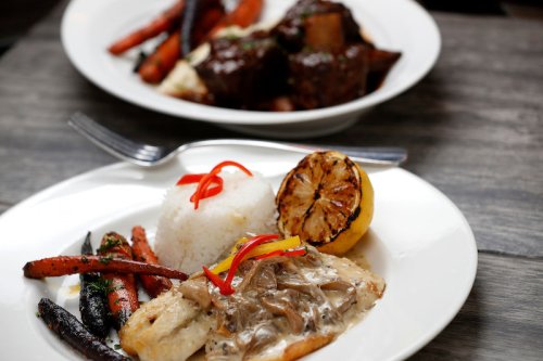 A plate of grilled fish with rice, colorful peppers, and roasted carrots, with a lemon slice on the side.
