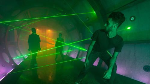 Three people in a dimly lit tunnel with green laser beams creating an atmospheric effect.