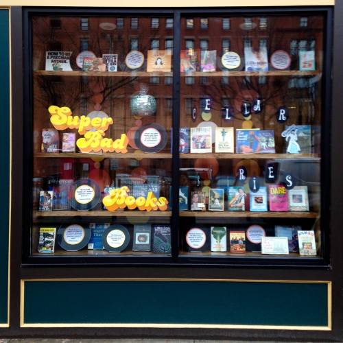 A bookstore window display featuring colorful signs and a variety of books arranged on shelves.