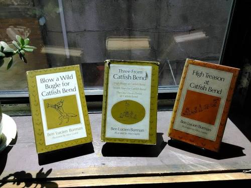 Three vintage books by Ben Lucien Burman titled "Blow a Wild Bugle for Catfish Bend," "Three from Catfish Bend," and "High Treason at Catfish Bend," displayed on a windowsill.