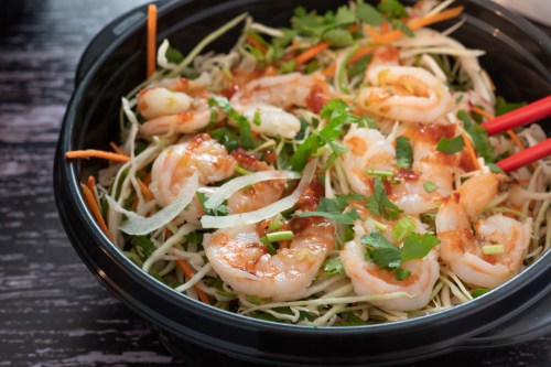 A black bowl filled with shrimp salad, featuring shrimp, cabbage, carrots, and fresh herbs, with chopsticks on the side.