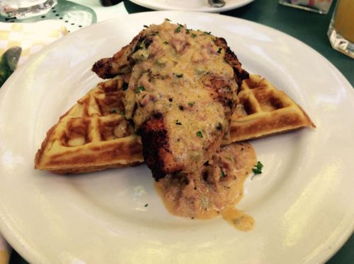A plate featuring a piece of chicken on waffles, topped with a creamy sauce and garnished with parsley.