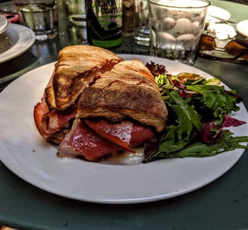 A sandwich with layers of meat and tomato, served on a plate with a side of mixed greens.