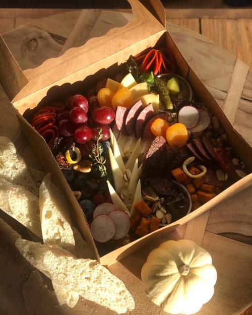 A beautifully arranged charcuterie box with meats, cheeses, fruits, nuts, and crackers, set on a wooden table.