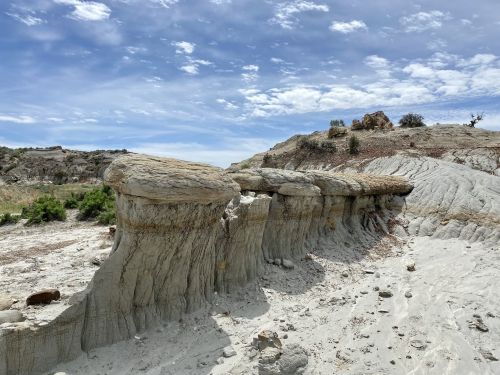 A rocky landscape featuring unique, layered formations under a blue sky with scattered clouds.