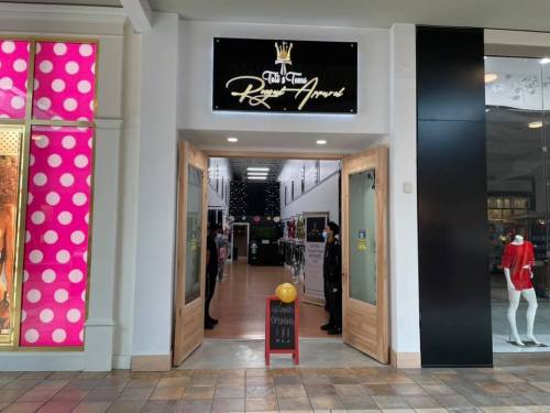 Entrance to a retail store with a sign above, flanked by two wooden doors and a chalkboard sign outside.