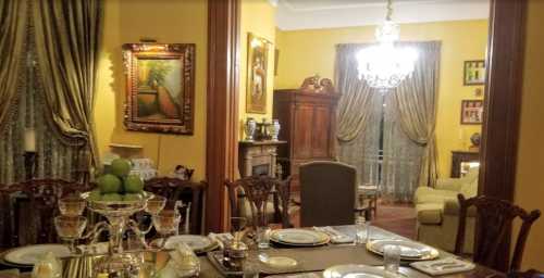 Elegant dining room with a set table, ornate decor, and a cozy living area visible in the background.