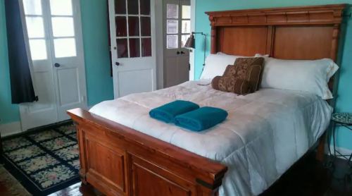 Cozy bedroom with a wooden bed, white bedding, and turquoise towels, featuring light blue walls and double doors.