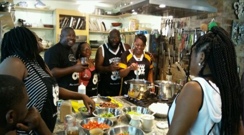 A group of people cooking together in a kitchen, surrounded by fresh ingredients and enjoying each other's company.