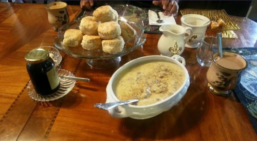 A wooden table set with biscuits, a bowl of soup, a jar of jam, and cups of tea.