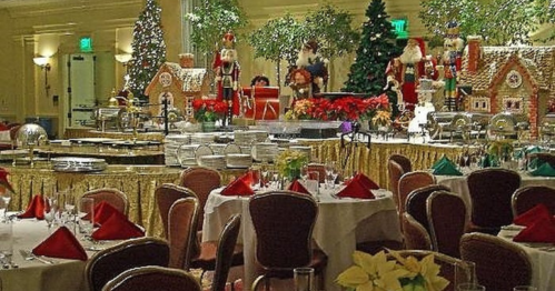 Festively decorated dining area with tables set for a holiday event, featuring Christmas trees and gingerbread displays.