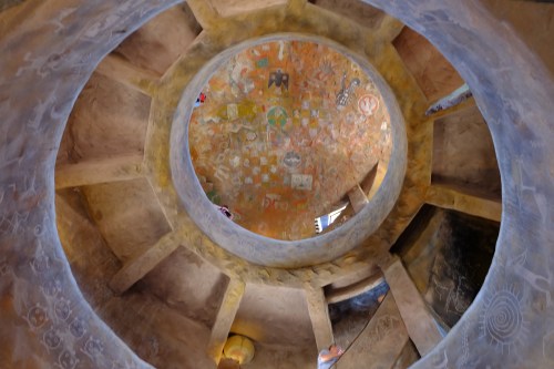 View from below of a circular, textured ceiling with colorful murals and intricate designs.