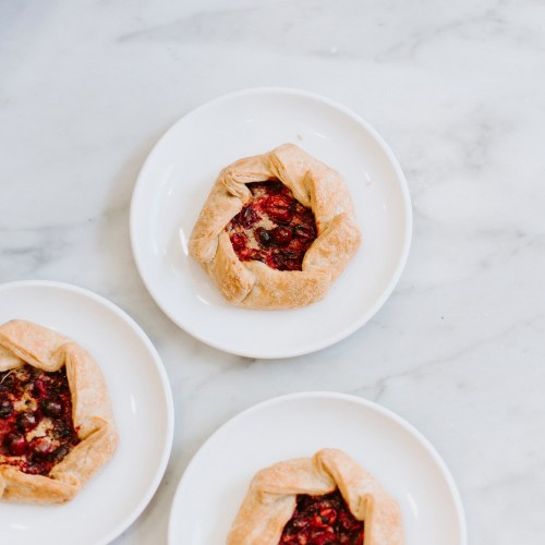 Three fruit galettes on white plates, arranged on a marble surface.