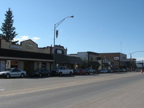 A street view of a small town with shops, parked cars, and clear blue skies.