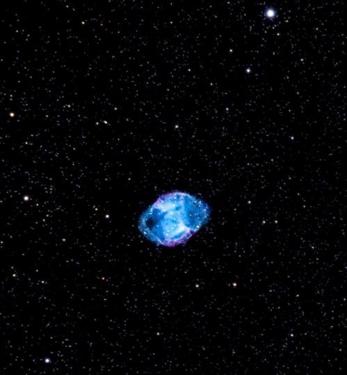 A vibrant nebula surrounded by stars, showcasing shades of blue and purple against a dark cosmic background.