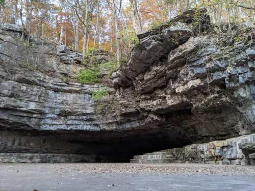 A large rock formation with a cave entrance, surrounded by trees and autumn foliage.