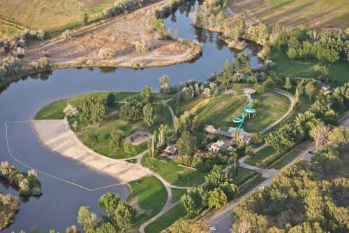 Aerial view of a park with a river, green trees, a sandy beach area, and water slides in the background.