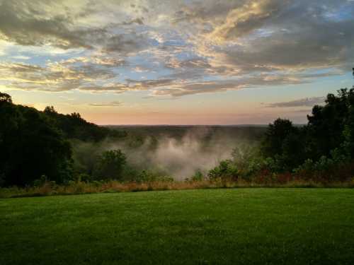 A serene landscape view of rolling hills shrouded in mist under a colorful sky at sunrise.