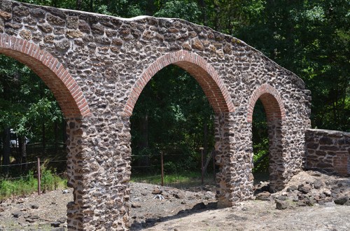 Stone arches with brick accents stand amidst greenery, showcasing historical architecture in a natural setting.