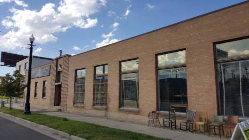 A brick building with large windows, featuring several chairs placed outside along a sidewalk under a cloudy sky.