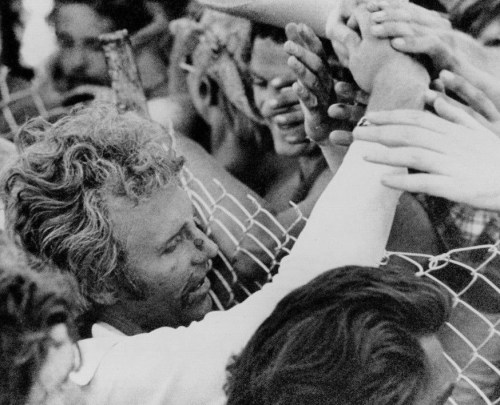 A crowd of people reaching through a fence, with hands grasping and faces expressing excitement and emotion.