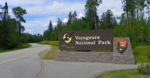 Sign for Voyageurs National Park along a winding road, surrounded by lush greenery and trees.