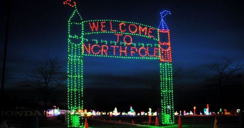 Colorful holiday lights form an archway that reads "Welcome to North Pole" against a dark evening sky.