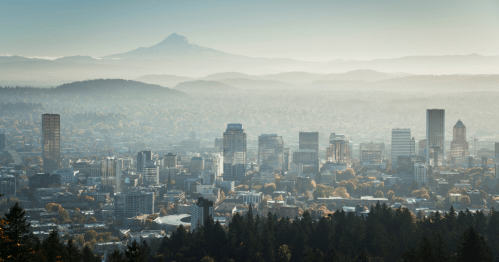 A panoramic view of a city skyline with mountains in the background, shrouded in mist and autumn foliage.