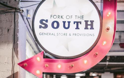Sign for "Fork of the South" General Store & Provisions, featuring a bright arrow and decorative lights.