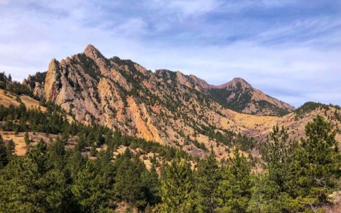 Scenic view of rugged mountains with colorful rock formations and green pine trees under a blue sky.