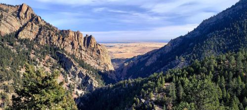 A scenic view of a valley between rocky mountains, surrounded by lush greenery and a clear blue sky.
