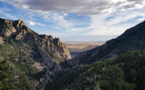 A scenic view of a valley surrounded by mountains, with trees and a cloudy sky above.