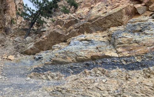 Rocky terrain with layered sedimentary rocks and sparse vegetation in a mountainous area.