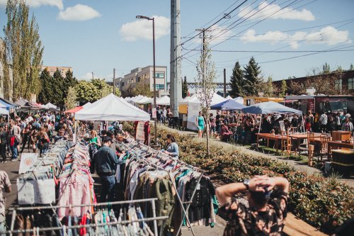 A bustling outdoor market with tents, clothing racks, and people enjoying the sunny day.