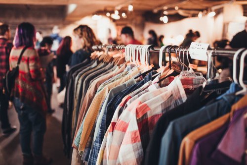 A rack of colorful shirts in a busy indoor market with people browsing in the background.