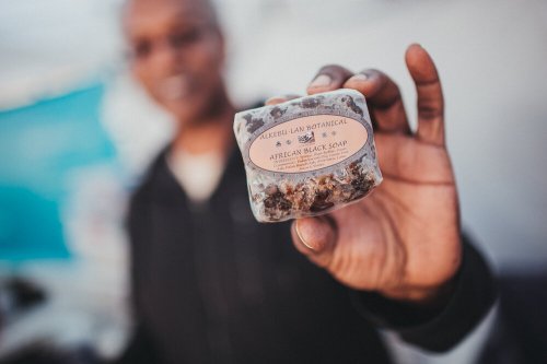 A person holds a bar of African black soap with a label, blurred background.