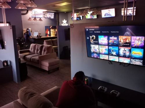 A cozy gaming lounge with a large TV displaying game options and a person sitting on a couch, focused on gaming.